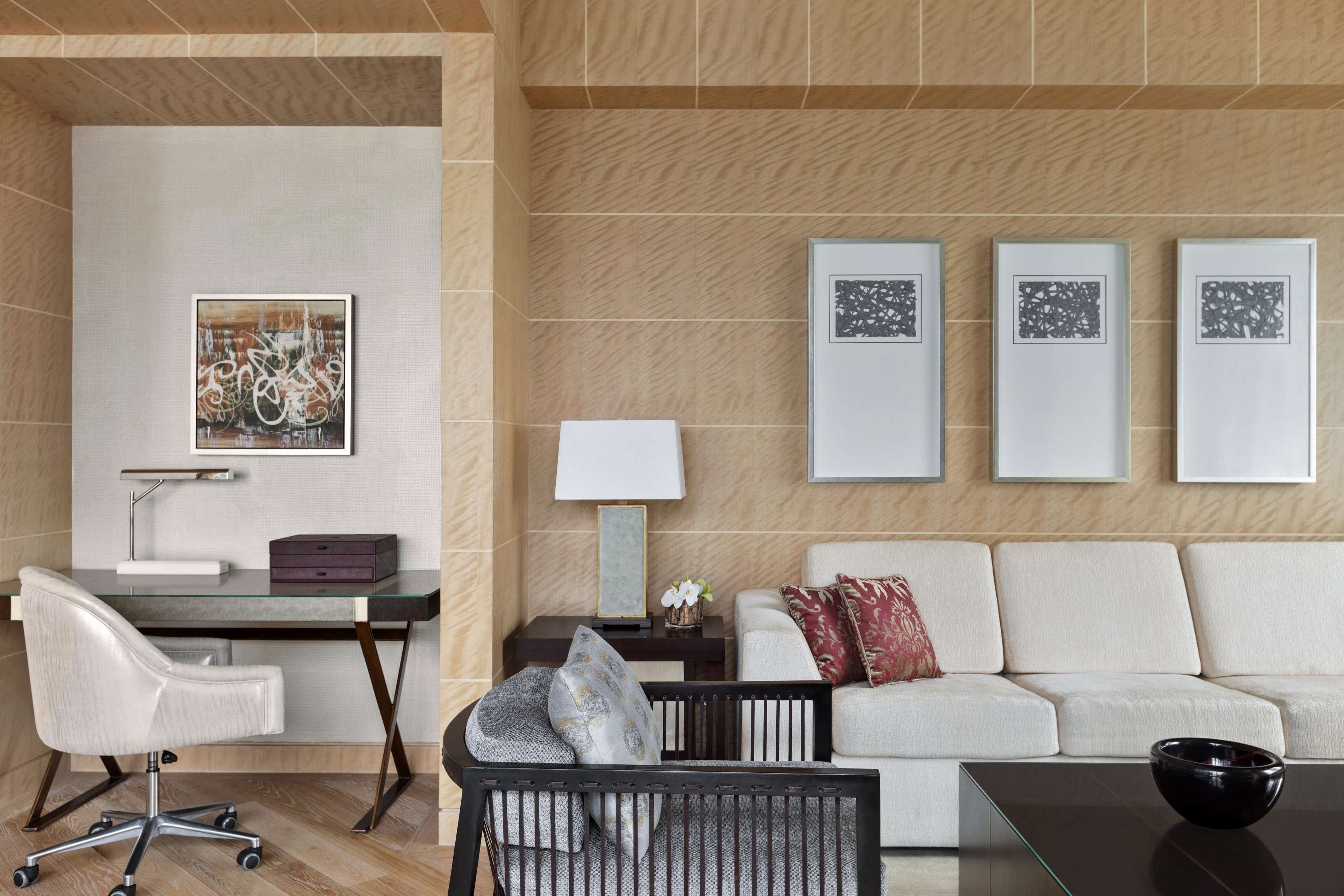 A modern room with a glass desk, a white sofa, and three framed artworks on the wall.