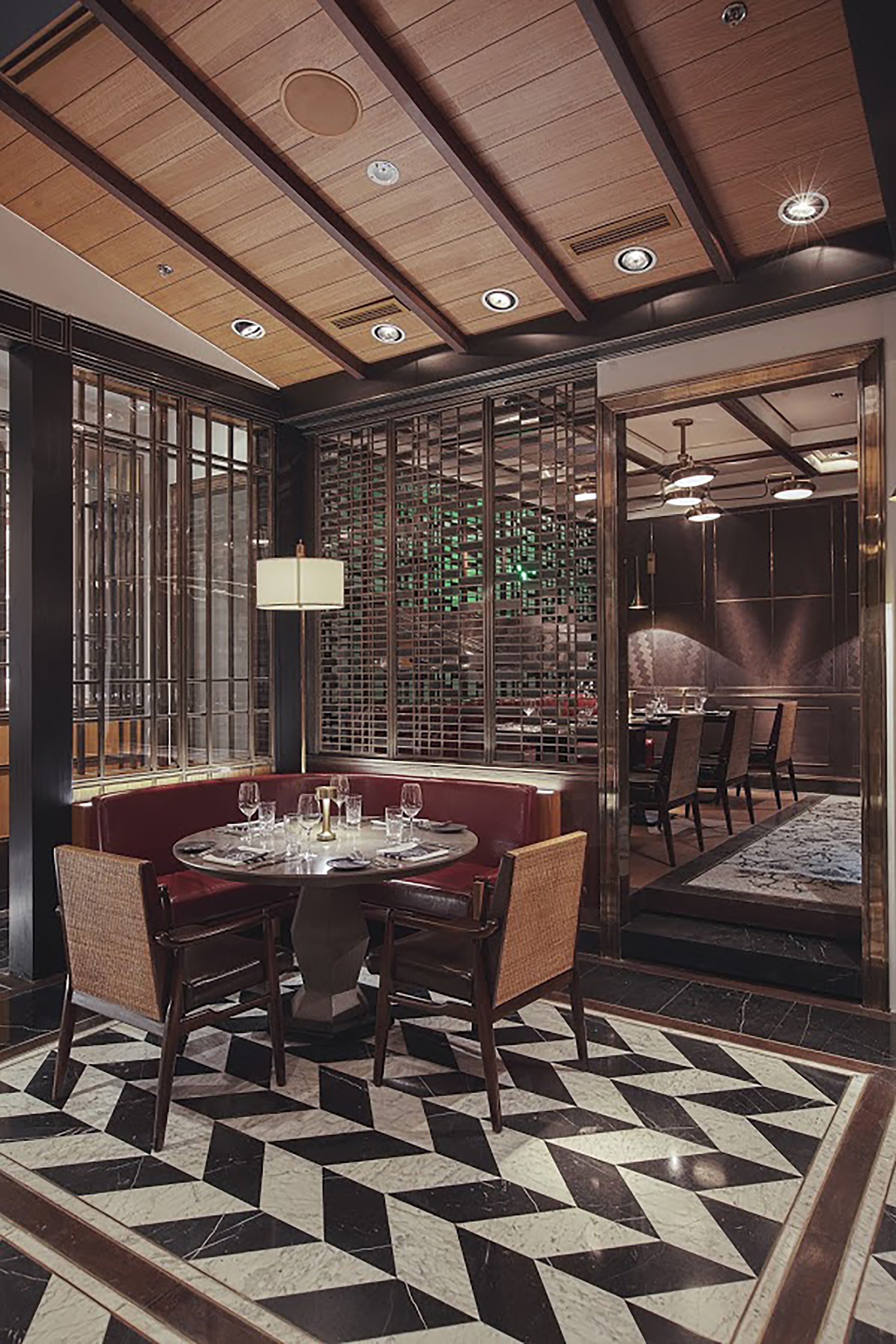 A dining area with a round table set for four, surrounded by cushioned chairs. The floor features a black and white geometric pattern.
