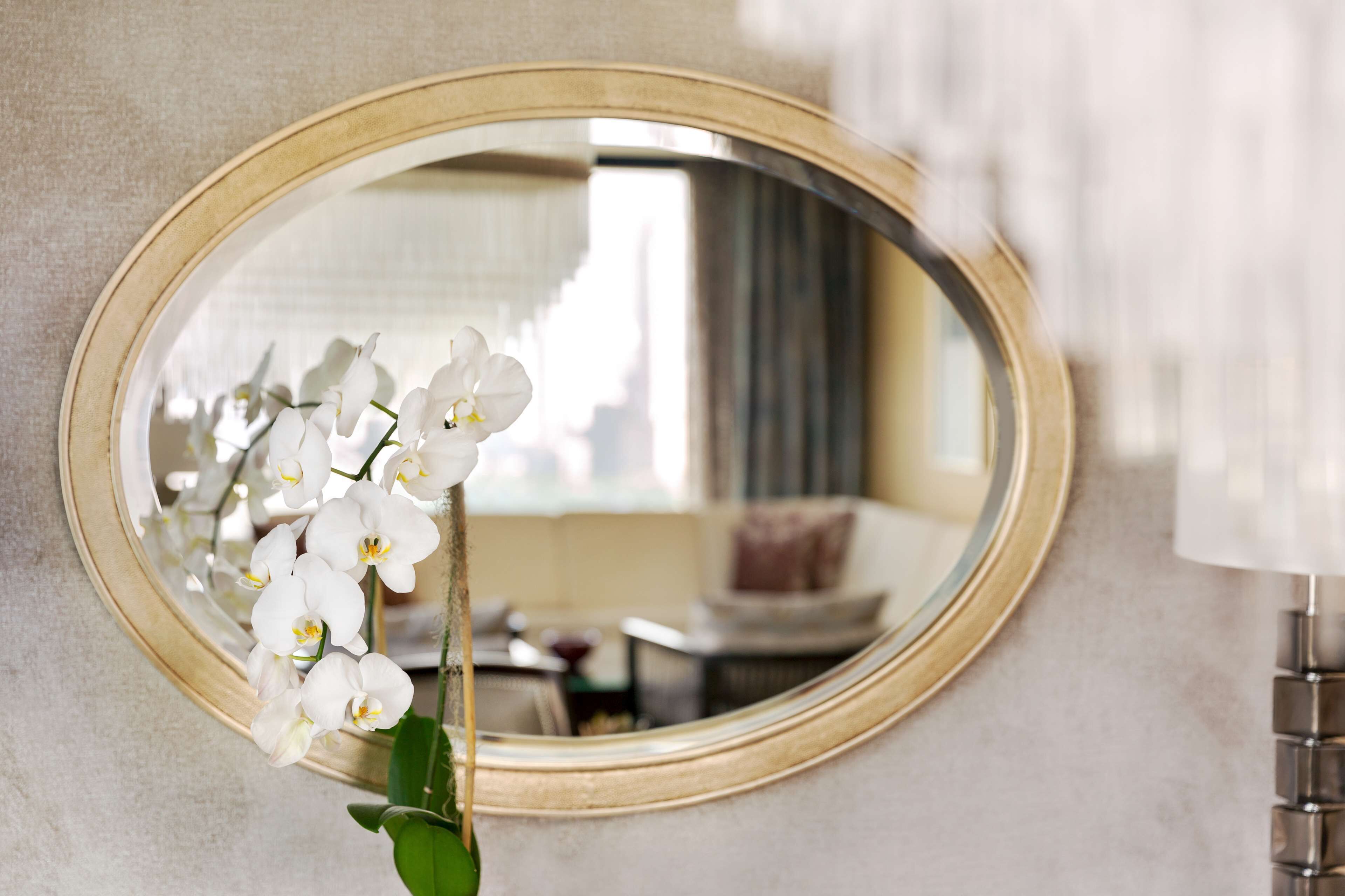 A mirror with a gold frame reflecting an orchid and a room interior.