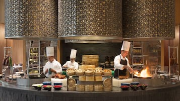 A professional kitchen with chefs preparing food, a display of various dishes, and a unique stone wall design.