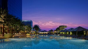 A swimming pool with lounge chairs and umbrellas, surrounded by palm trees and a modern building. - Shangri-La The Fort, Manila (Taguig)