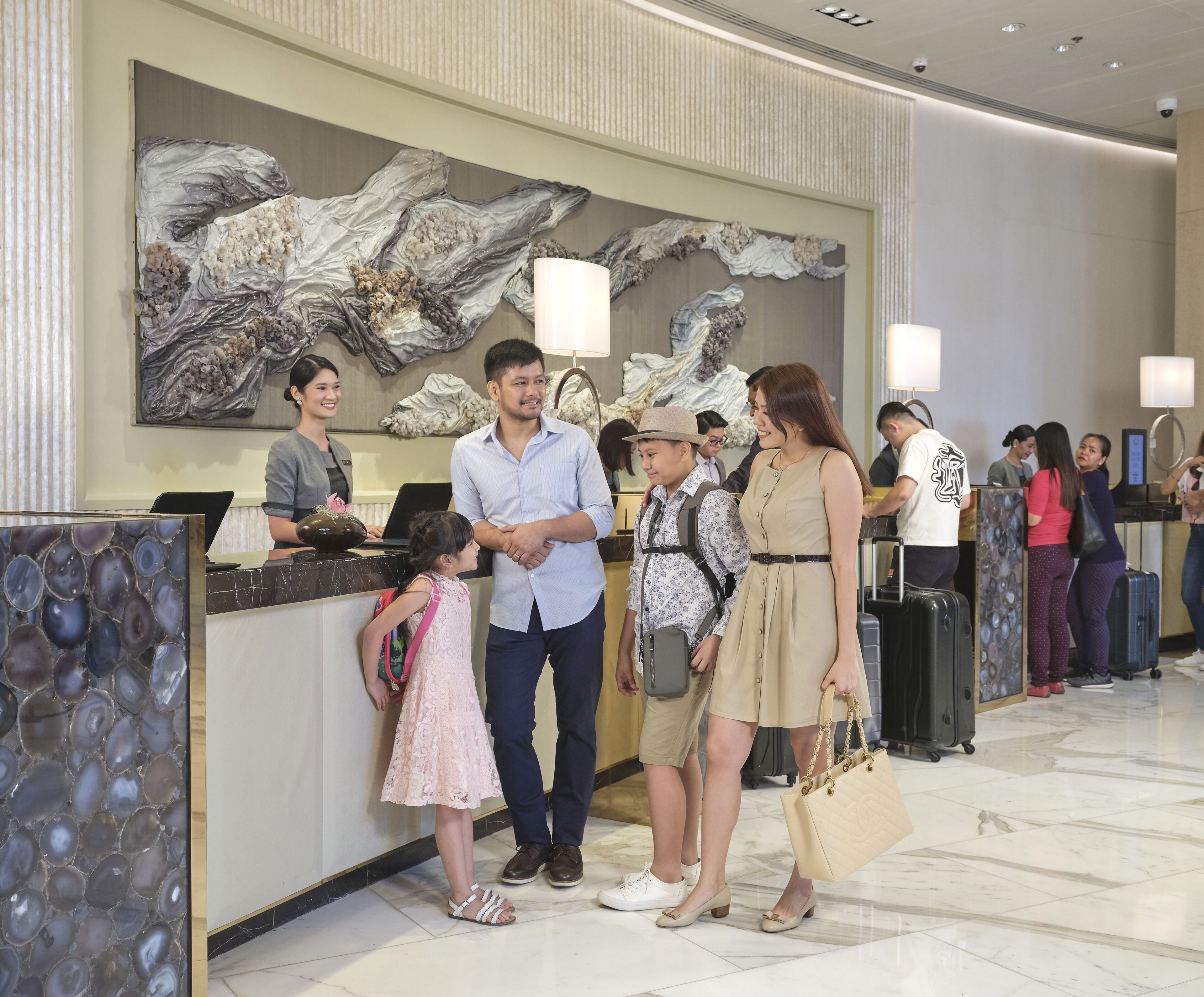 A hotel reception area with a marble reception desk, a large abstract wall art piece, and a modern ceiling design.