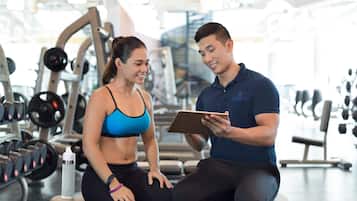 A gym with various exercise equipment and a person sitting on a bench.