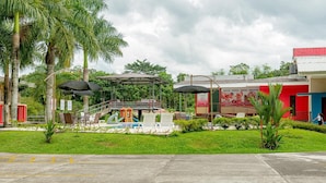 A pool area with a children's play structure, surrounded by palm trees and a building with a red and blue facade.