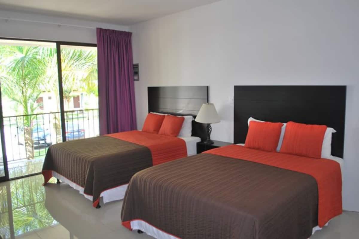 Habitación de hotel con dos camas, un balcón y vistas a palmeras.