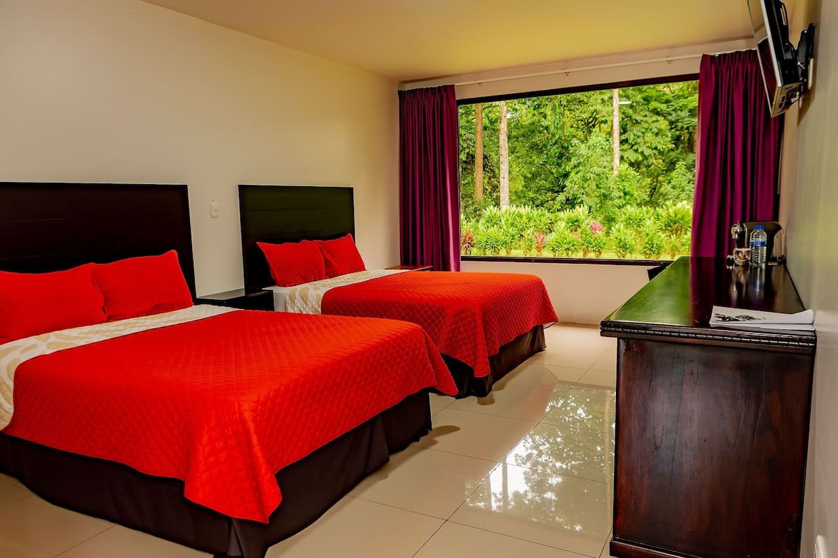Habitación de hotel con dos camas, un escritorio y una ventana con cortinas.