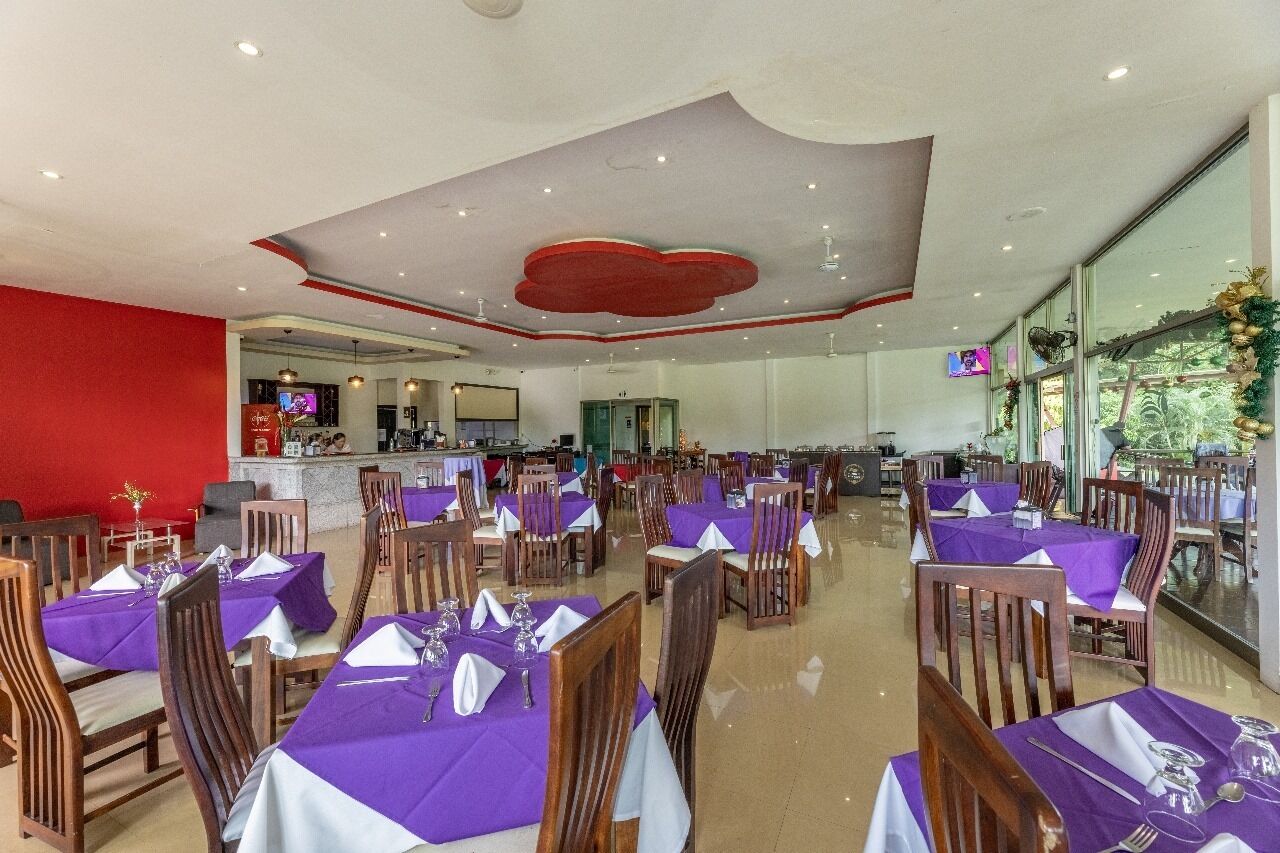 A spacious dining area with multiple tables and chairs, a bar area, and large windows offering a view of the outdoors.