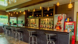 A bar area with a long counter, multiple stools, and a refrigerator stocked with beverages.