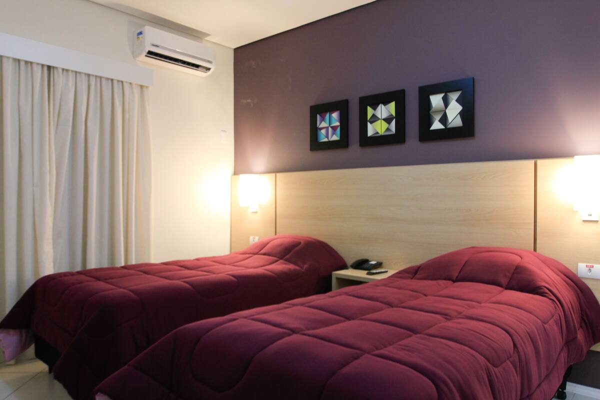 A hotel room with two beds, a nightstand, and a wall-mounted air conditioner.