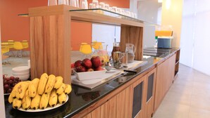 Un bufé de desayuno con frutas, dispensador de jugo y cafetera.