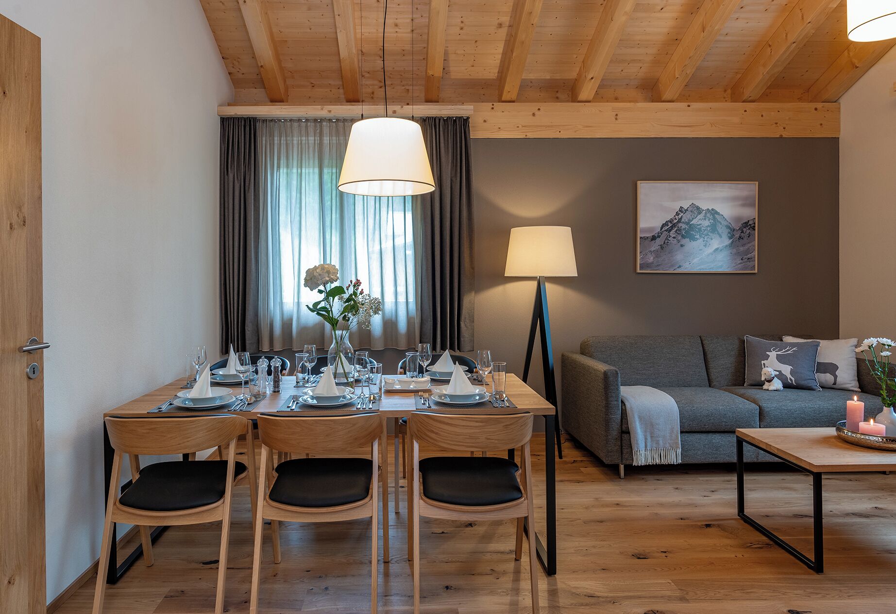 A dining area with a wooden table set for four, a sofa, and a lamp.