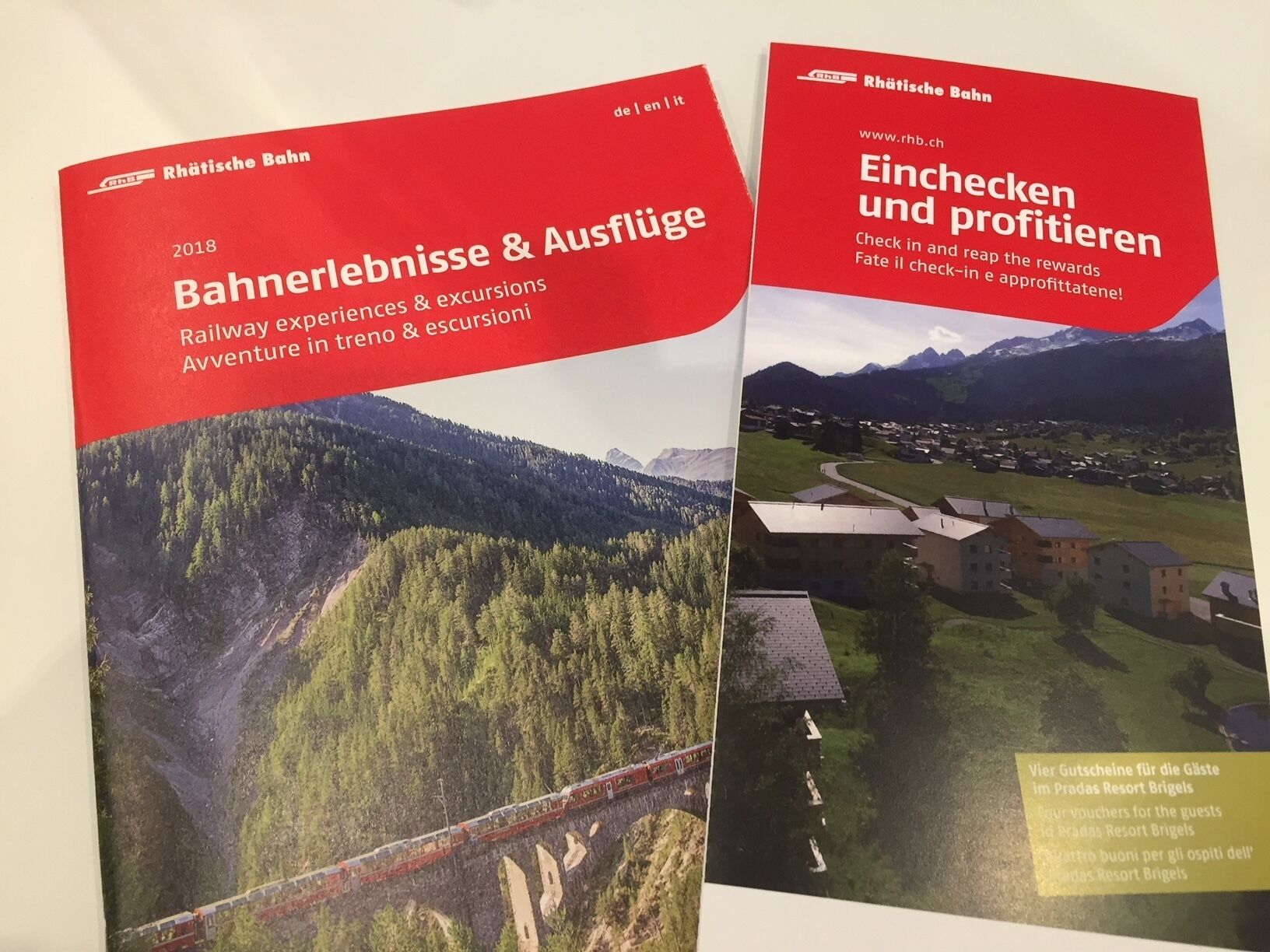 Dos fulletons de Rhaetische Bahn que destaquen experiències i excursions en tren, i una oferta promocional per a clients de Pradas Resort Brigels.