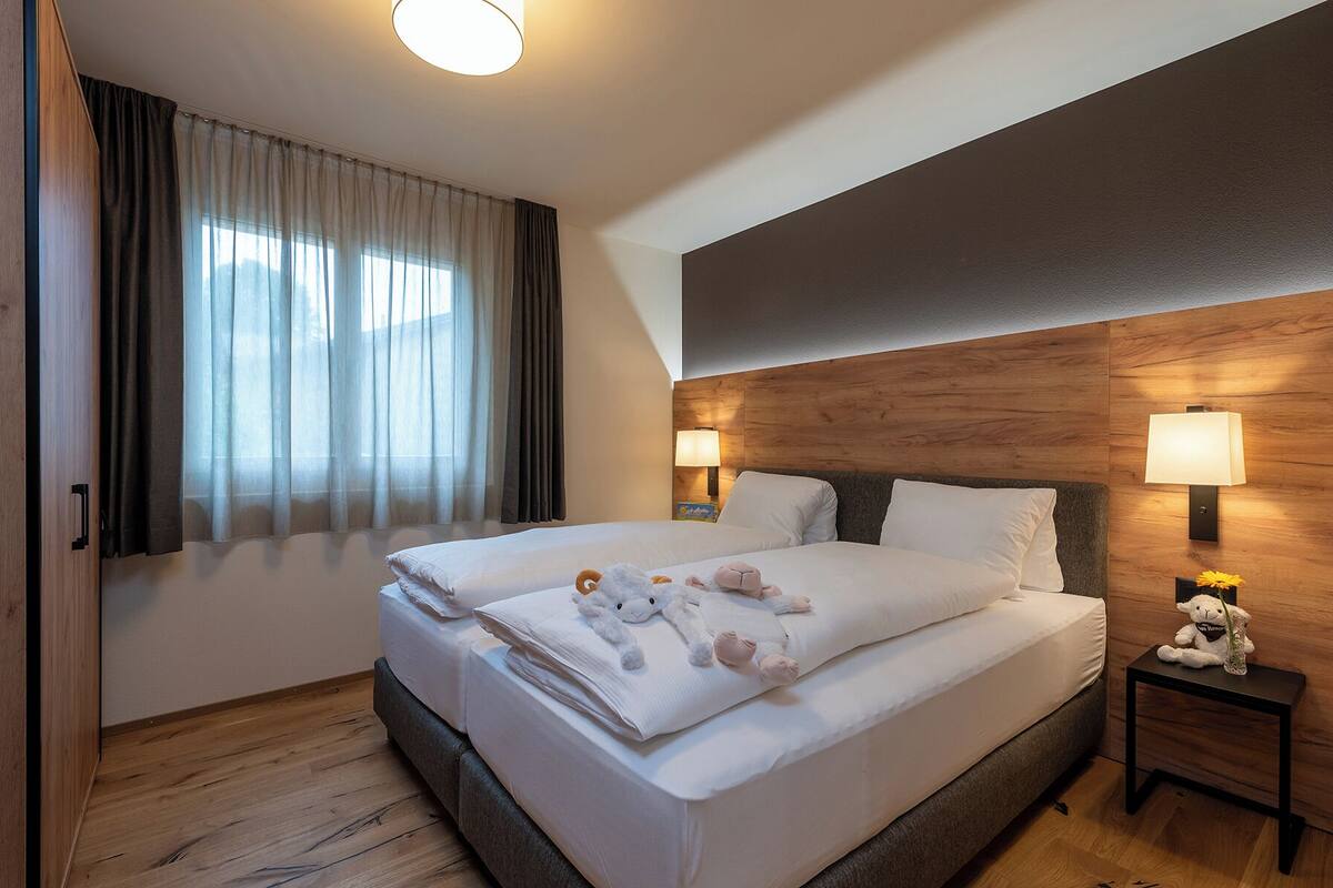 Quarto de hotel com uma cama grande, duas luminárias de cabeceira, uma cabeceira de madeira e uma janela com cortinas.