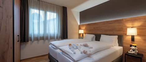 Une chambre d’hôtel avec un grand lit, deux lampes de chevet, une tête de lit en bois et une fenêtre avec des rideaux.