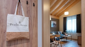 A room with a wooden ceiling, a sofa, a table with chairs, and a window with curtains. - Pradas Resort Brigels (Brigels)