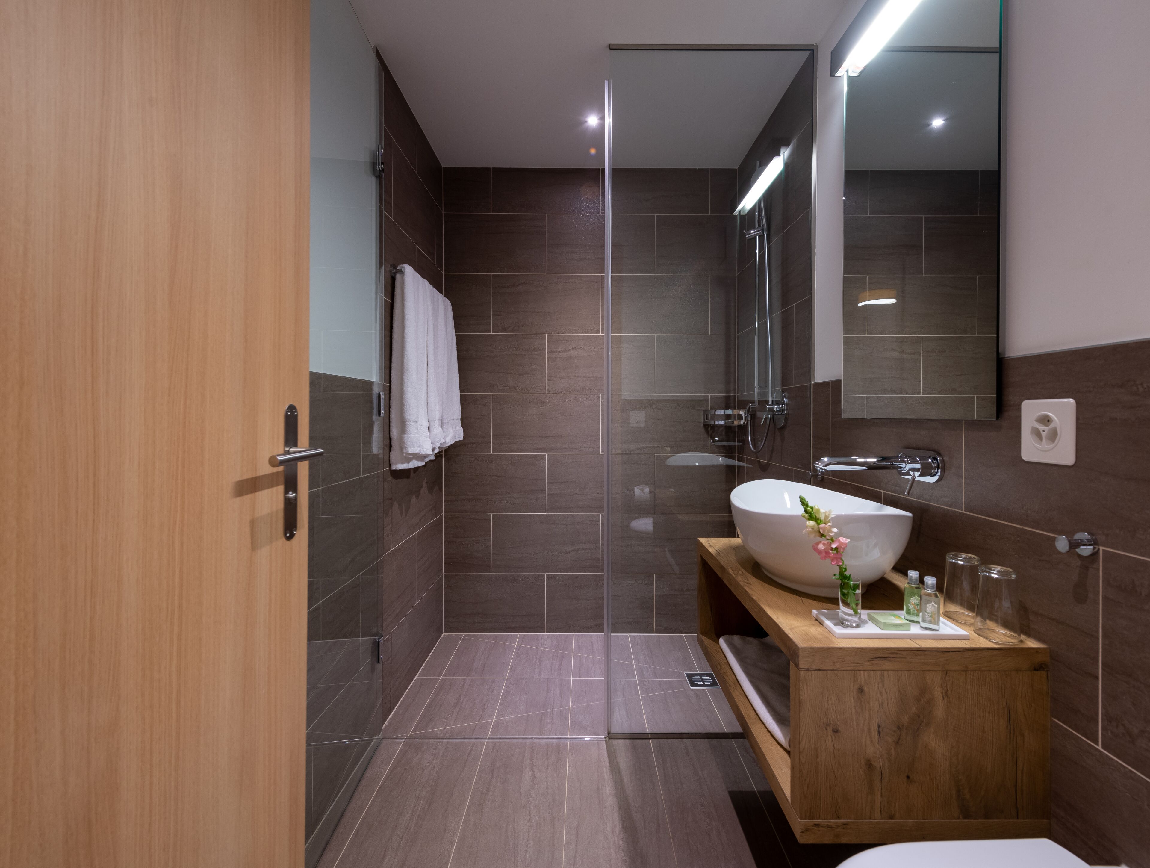 Un baño moderno con tocador de madera, un espejo grande y zona de ducha.