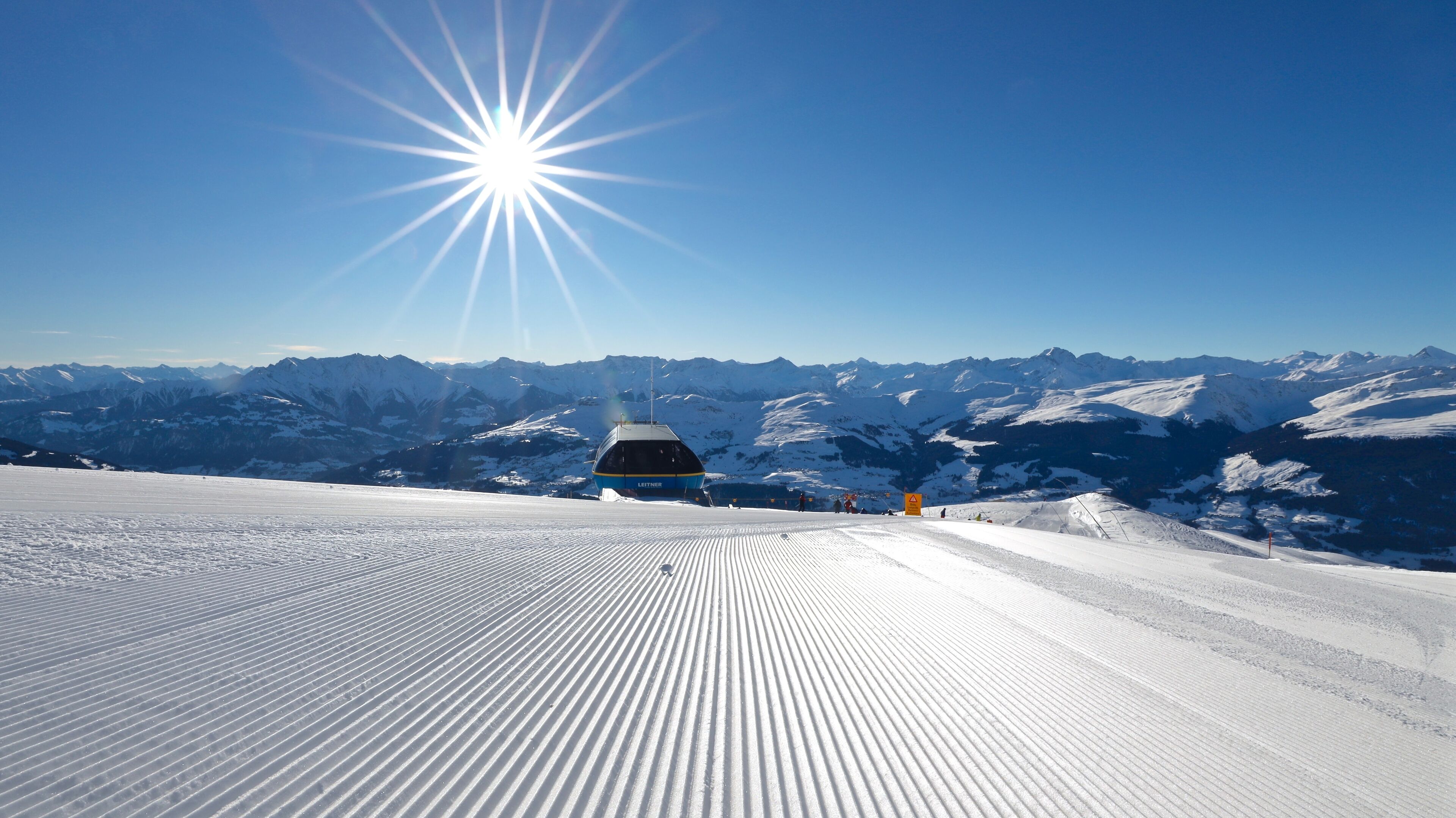 A snow-covered ski slope with a ski lift and mountains in the background.