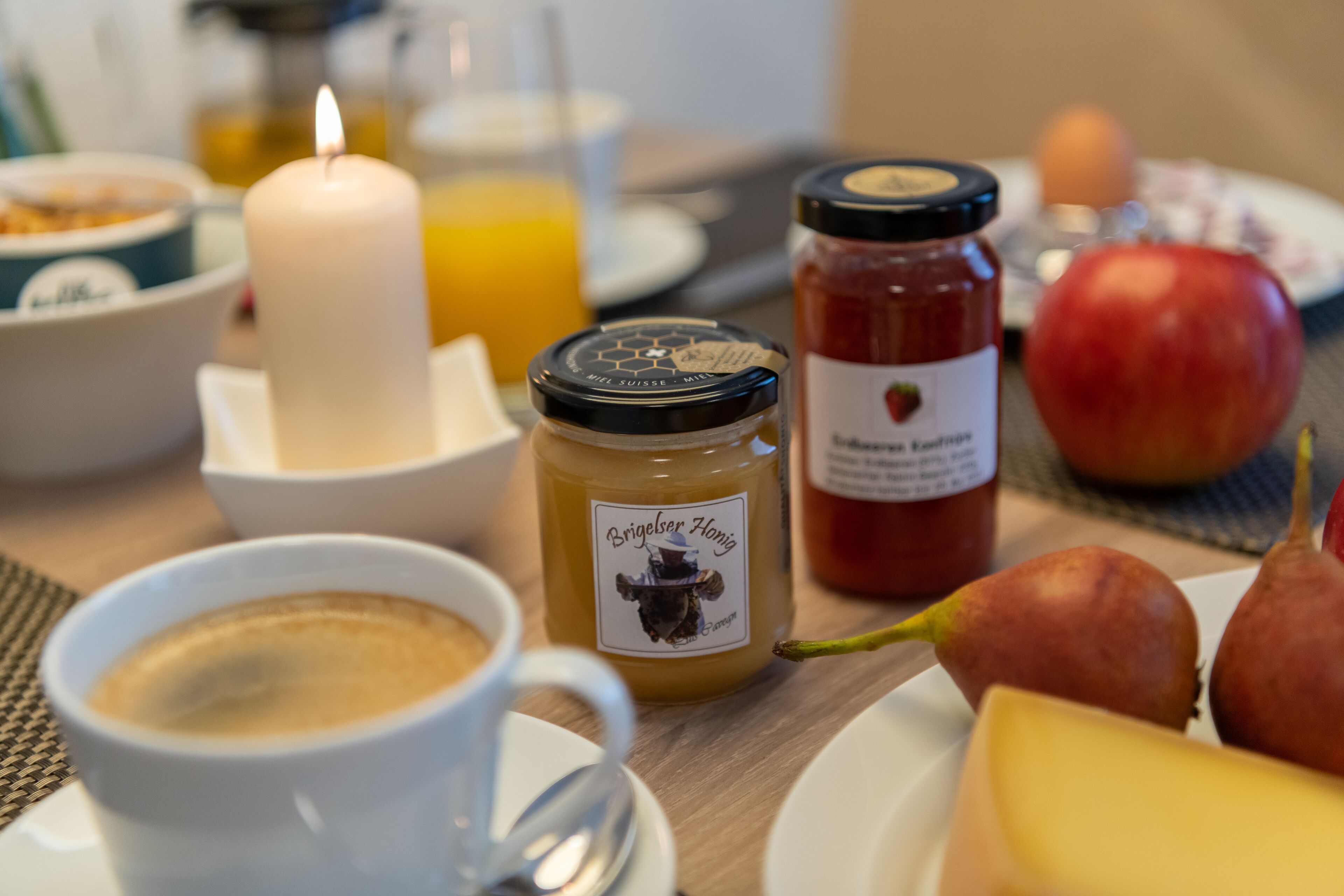 Frühstücksauslage mit Kerze, Kaffeetasse, Honigglas, Apfel, Birne und Orangensaft.