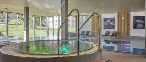 Un área de piscina interior moderna con diseño circular, paredes de vidrio transparente y techo de madera.