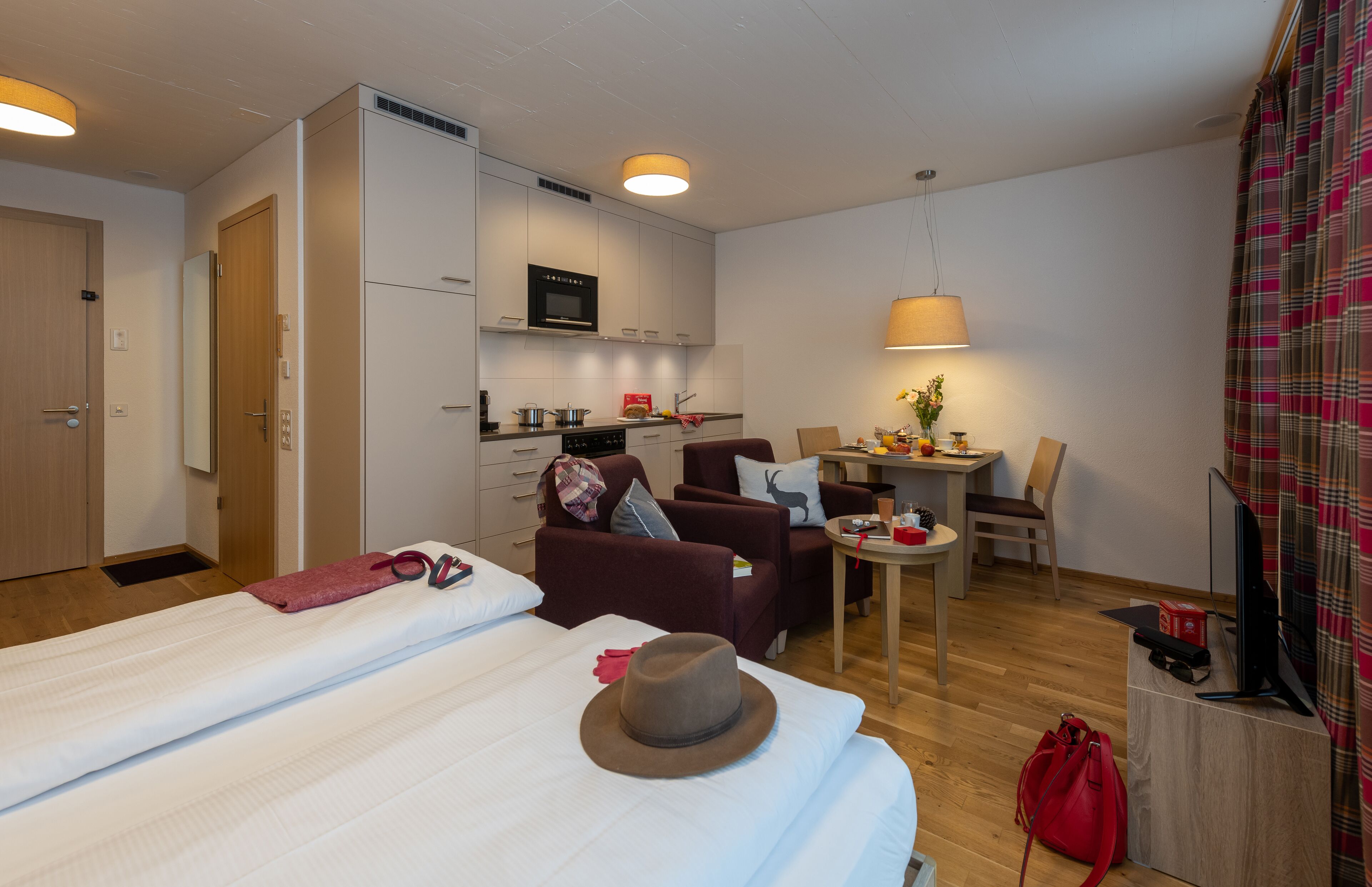 A compact hotel room with two beds, a kitchenette, a dining area, and a TV.