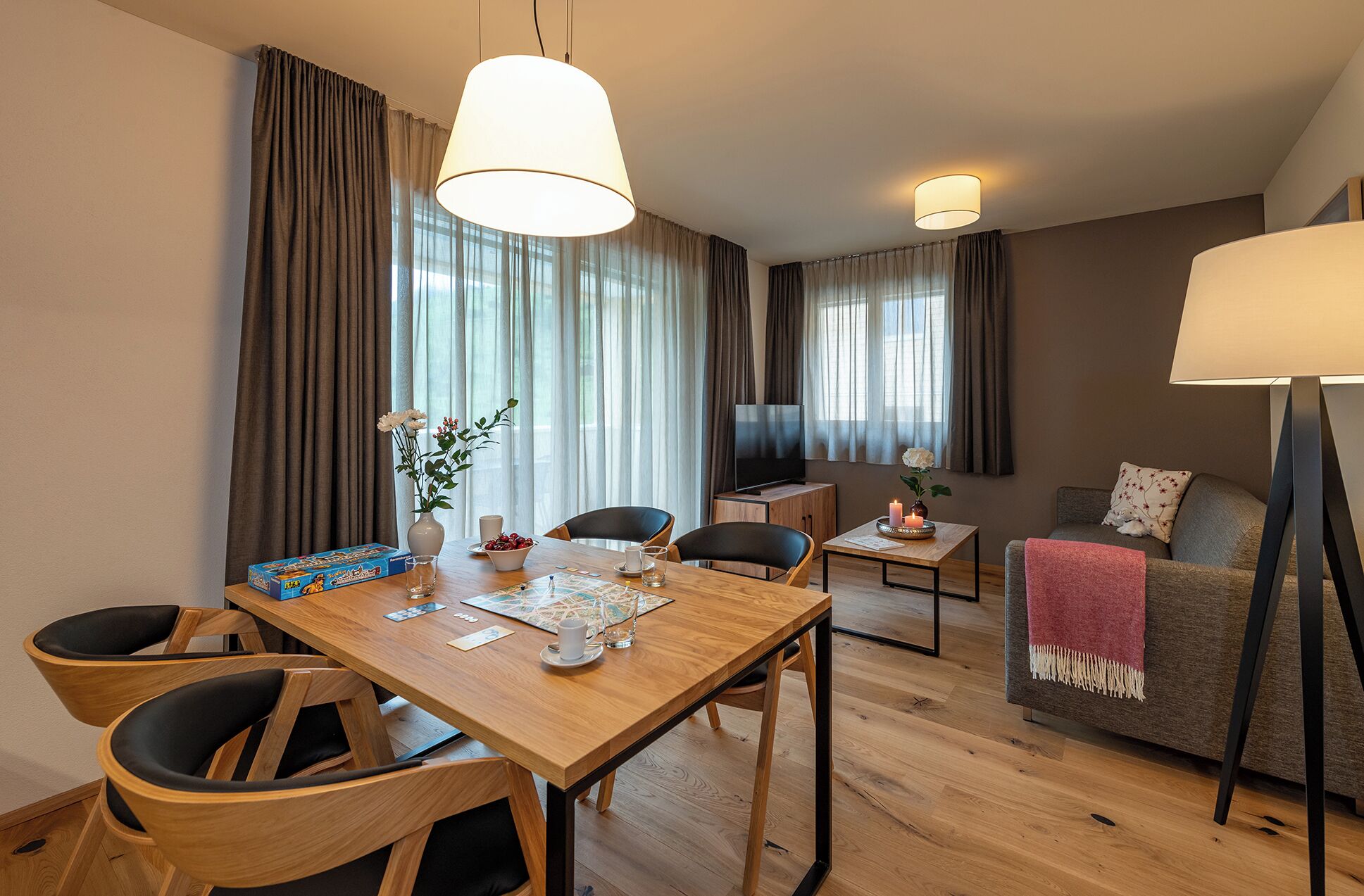 A modern living room with a wooden dining table, two chairs, a sofa, and a TV.