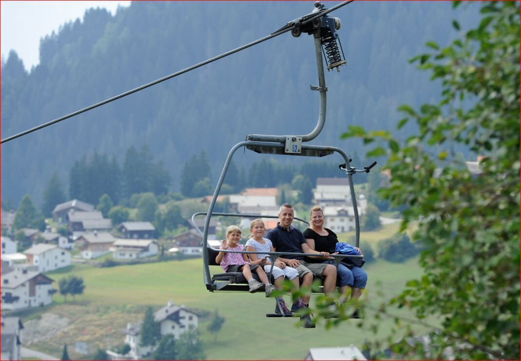 A family on a cable car with a mountainous village in the background.