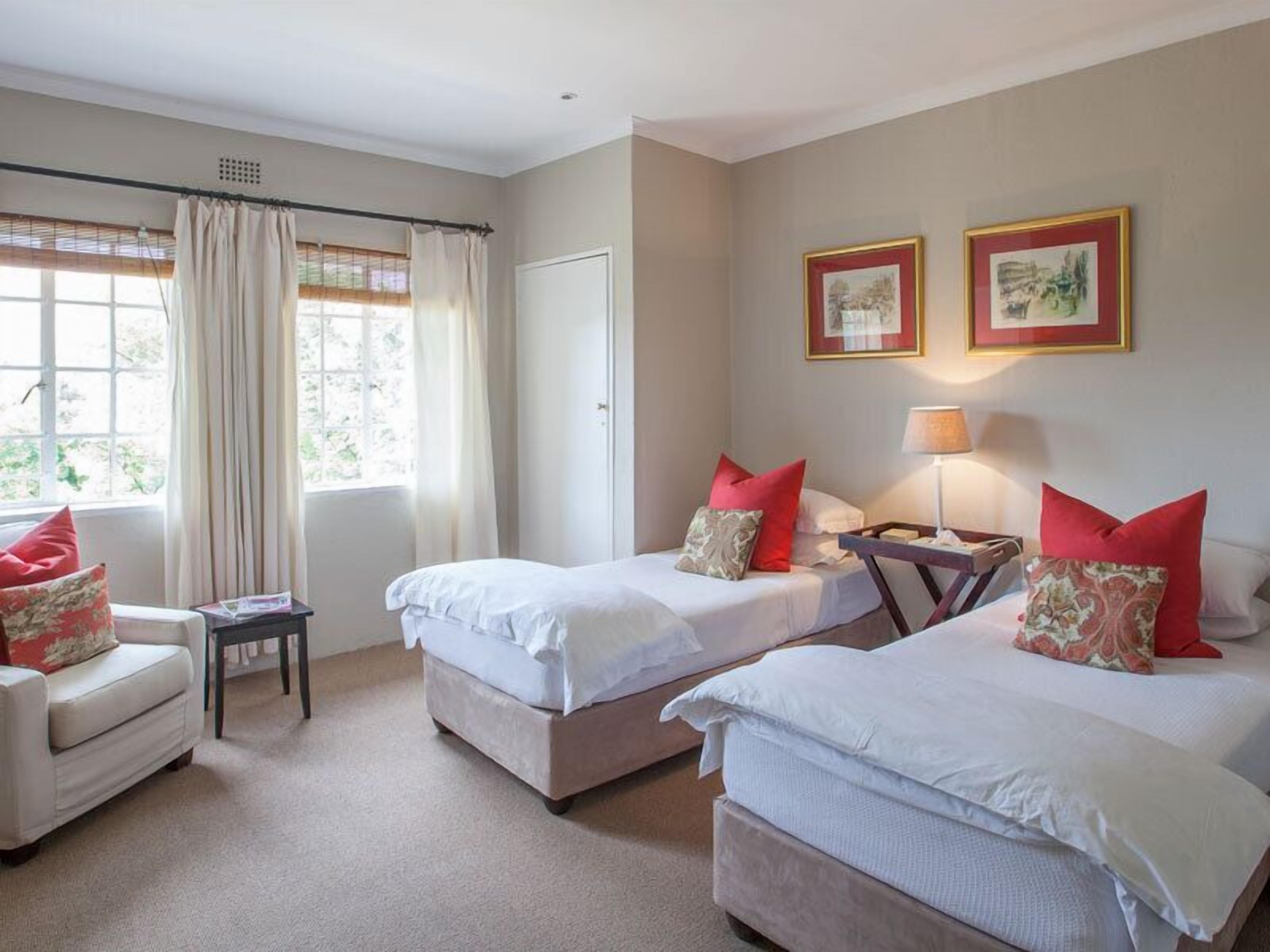 A hotel room with two beds, a small table, a chair, and a window with curtains.