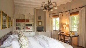 Une chambre à coucher avec un grand lit, un bureau avec une chaise, une bibliothèque et un lustre.