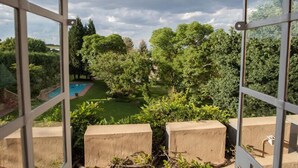 Une vue à travers une fenêtre, avec une piscine et une végétation luxuriante en arrière-plan.
