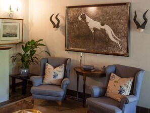 Quarto com duas poltronas, um quadro com um cão e um vaso com planta.