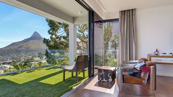 Ein moderner Balkon mit Blick auf einen Berg, eine Glastür, die zu einem Raum mit einer Couch und einem kleinen Tisch führt.