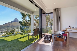 A modern balcony with a view of a mountain, a glass door leading to a room with a sofa and a small table. - Sea Star Rocks (Cape Town)