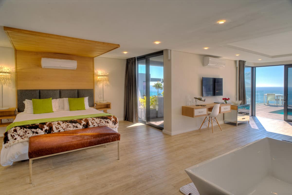 Ein modernes Hotelzimmer mit einem großen Bett, einem Schreibtisch, einem Sessel, einer Badewanne und einem Balkon mit Meerblick.