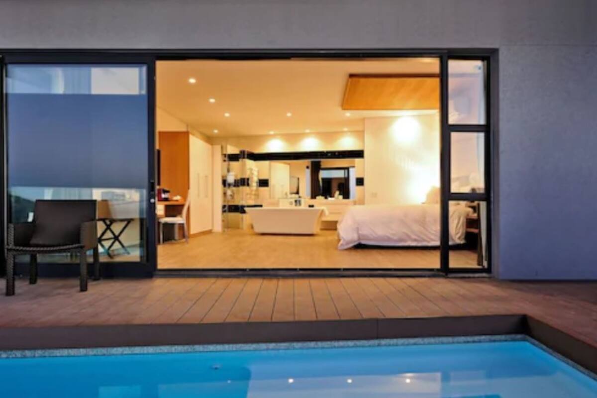 Ein modernes Hotelzimmer mit einer großen Schiebeglasdoor zum Balkon, einem separaten Badezimmer und einem Poolbereich.