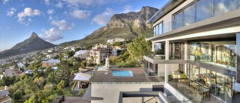 A modern building with a rooftop pool, glass balconies, and a view of a mountain.