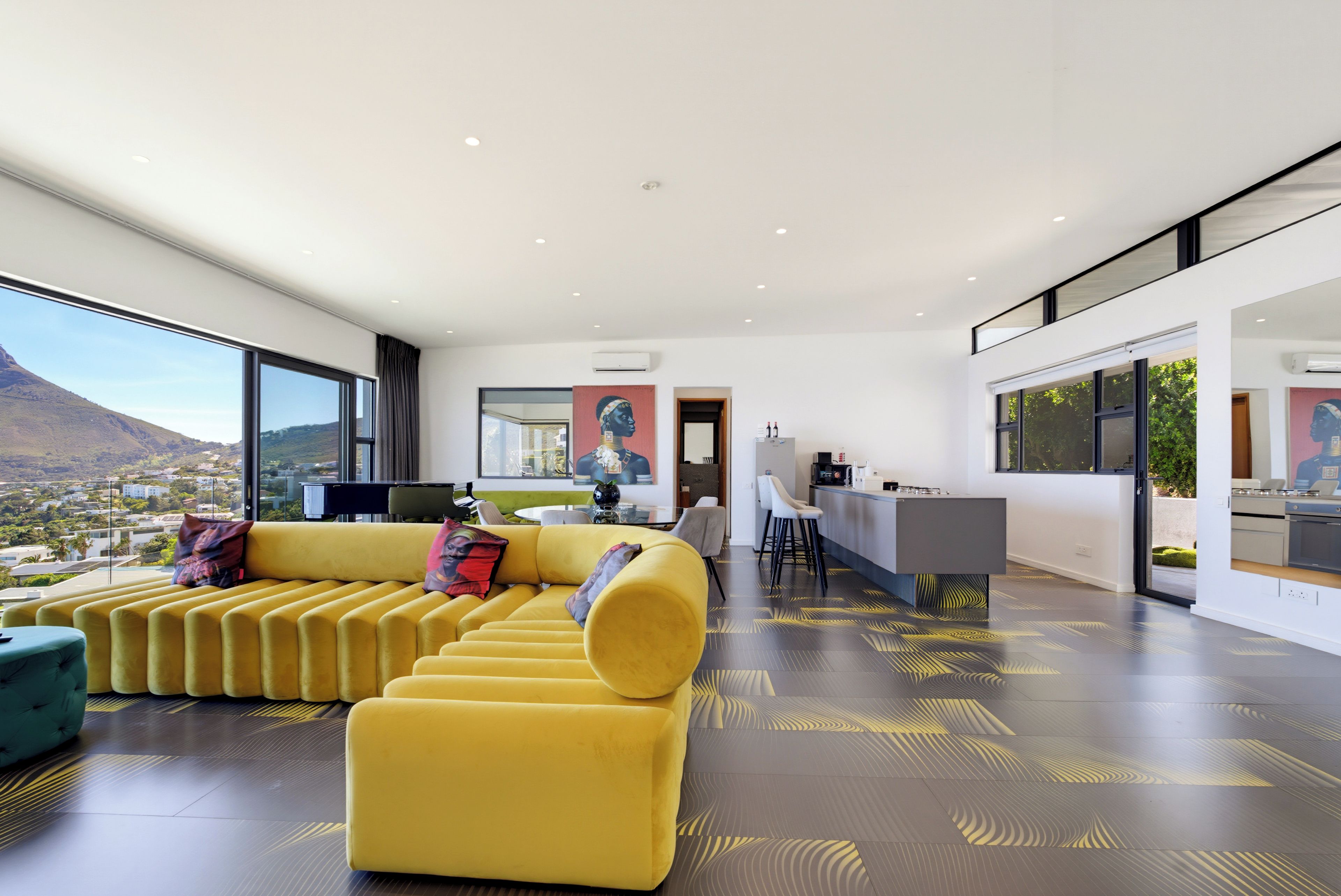 A modern living room with a yellow sofa, a dining area, and a kitchen.