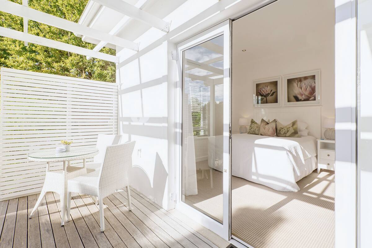 A bedroom with a glass door leading to a balcony, a bed with white bedding, and two framed pictures on the wall.