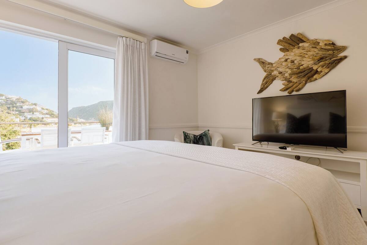 A hotel room with a large bed, a flat-screen TV, a decorative fish wall art, and a view of the outdoors.