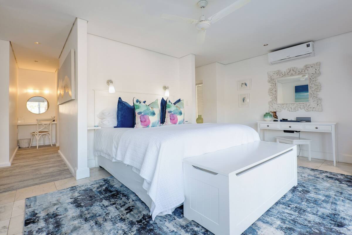 A modern bedroom with a white bed, a desk, and an air conditioning unit.