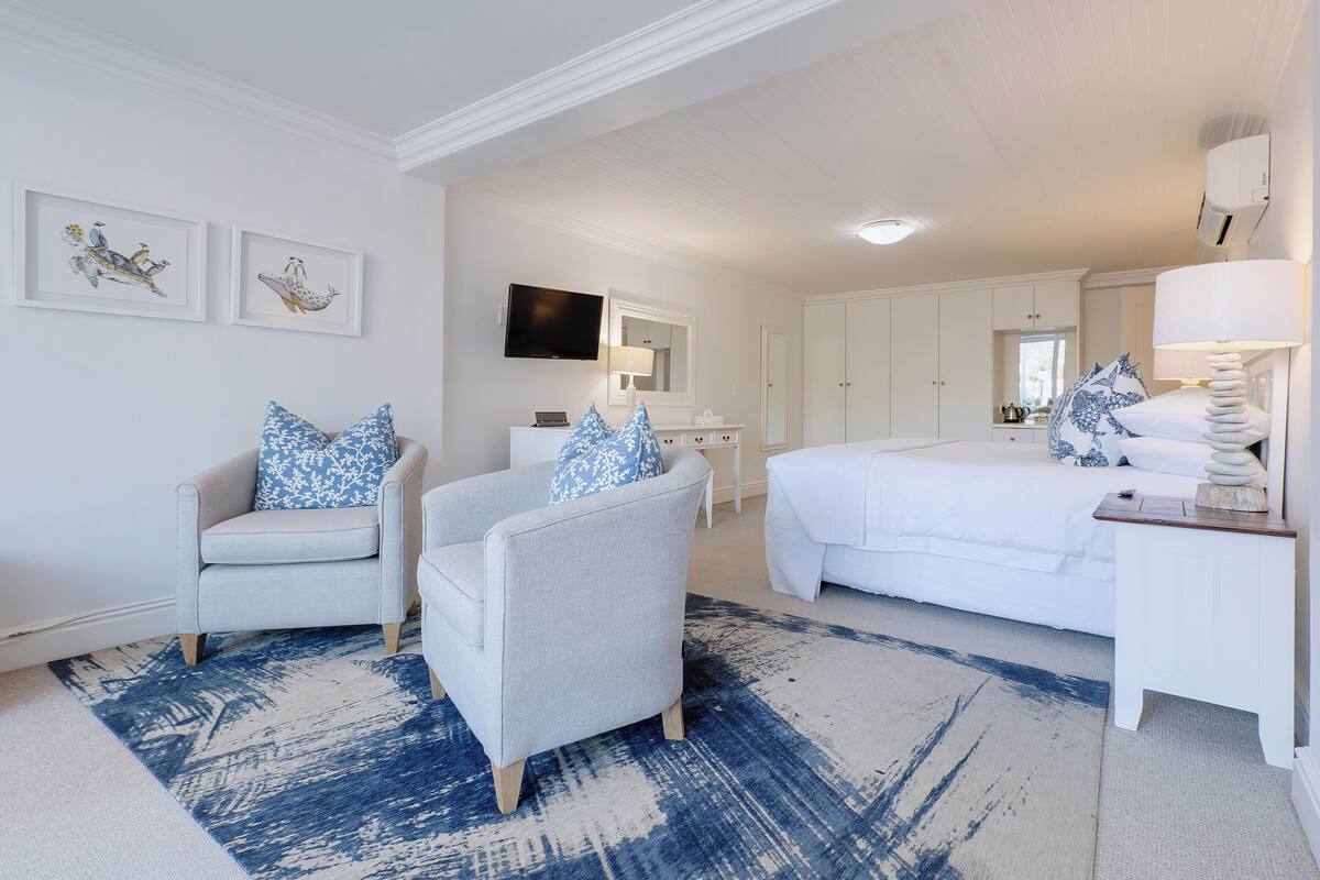 A hotel room with a bed, two armchairs, a desk, and a TV.