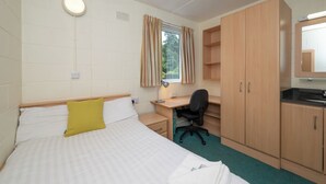Een kamer met een bed, bureau, stoel en spiegel.