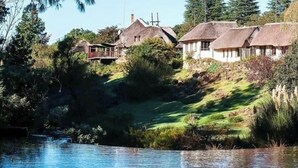 A riverside property with thatched-roof cottages, a grassy embankment, and a calm water body. - Hawklee Country House (Fort Nottingham)
