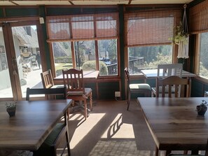 A cozy restaurant with wooden tables and chairs, large windows with bamboo blinds, and a view of the outdoor patio area. - Hawklee Country House (Fort Nottingham)