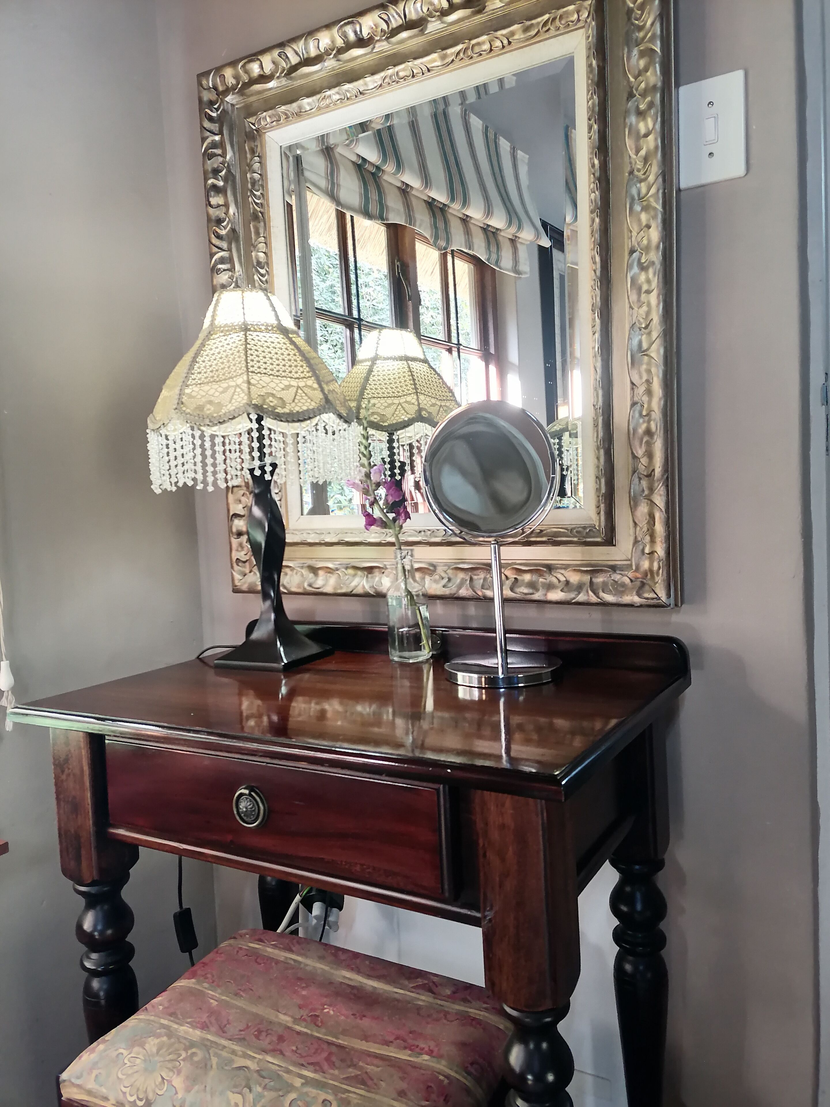 Une coiffeuse en bois avec un miroir, deux lampes et un vase de fleurs.