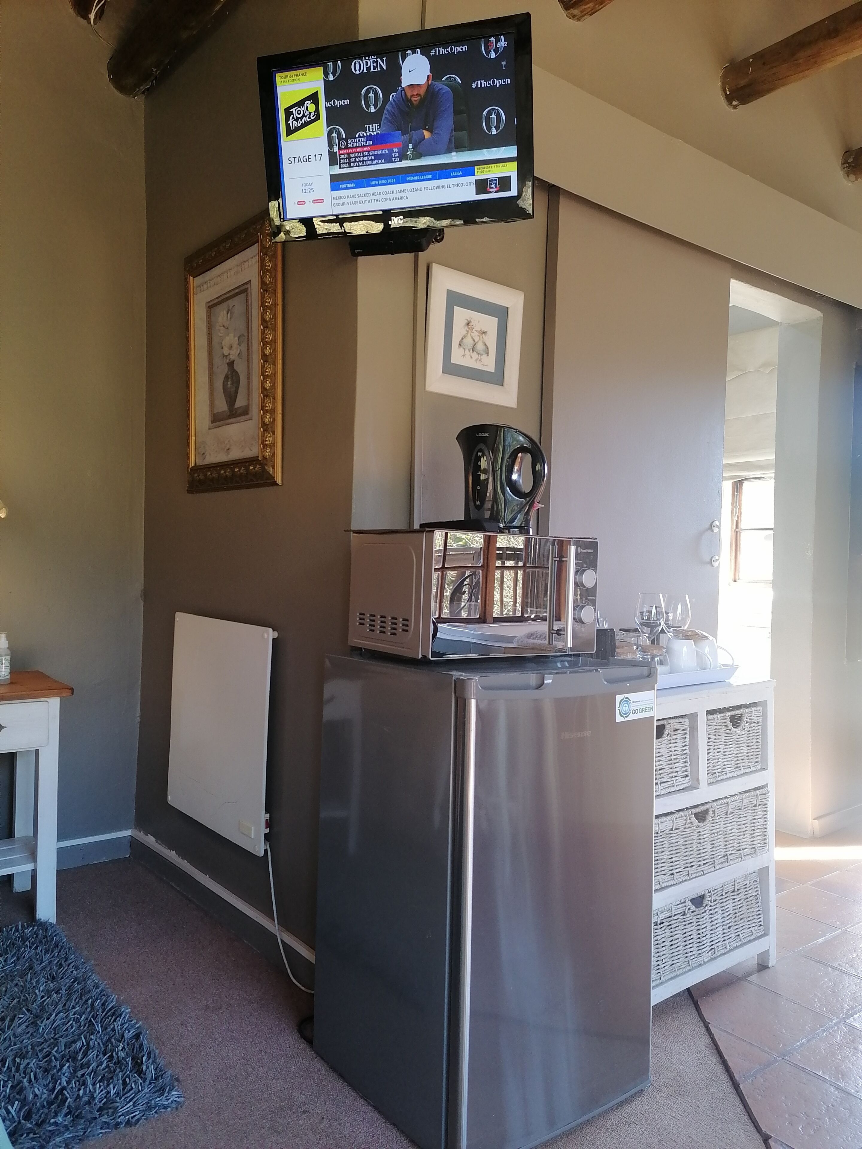 A kitchen with a stainless steel refrigerator, a coffee maker, and a television mounted on the wall displaying a sports event.