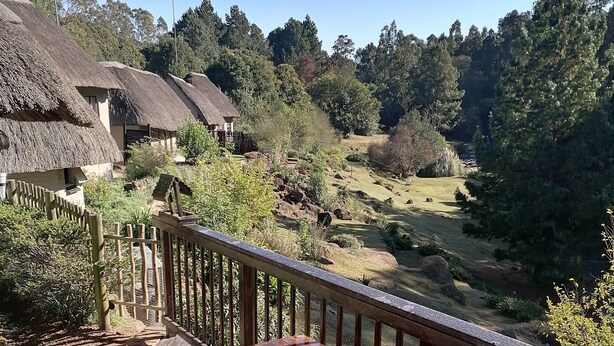 A wooden deck with a table and chairs, overlooking a rural landscape with thatched-roof buildings and greenery. - Hawklee Country House (Fort Nottingham)