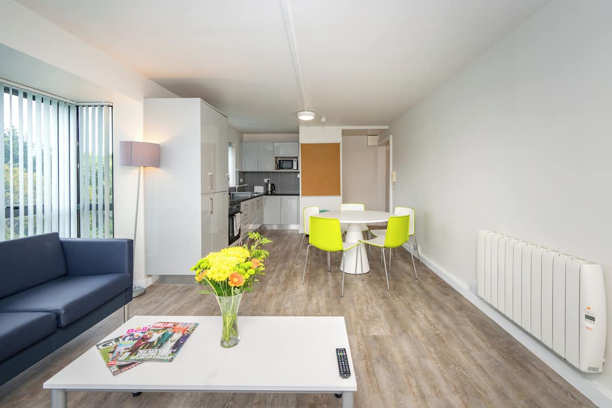 Una sala moderna con un sofá, una mesa de centro con una revista, un florero con flores y un comedor con una mesa y sillas.