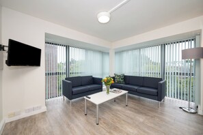 Una sala de estar moderna con un sofá azul oscuro, una mesa de centro blanca con un jarrón de flores y un televisor de pantalla plana montado en la pared.