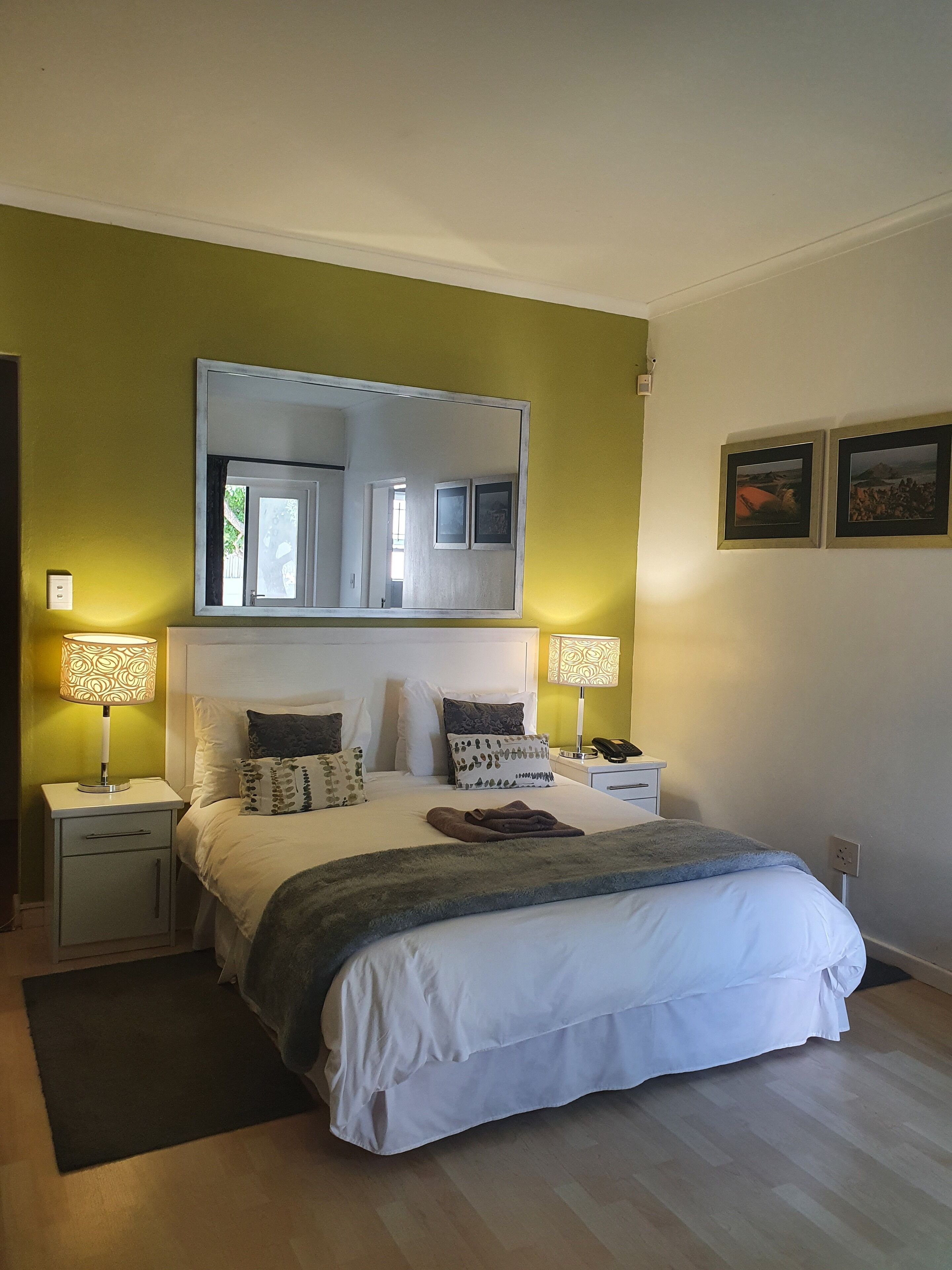 A bedroom with a bed, two bedside tables, a nightstand, a mirror, and two wall-mounted lamps.