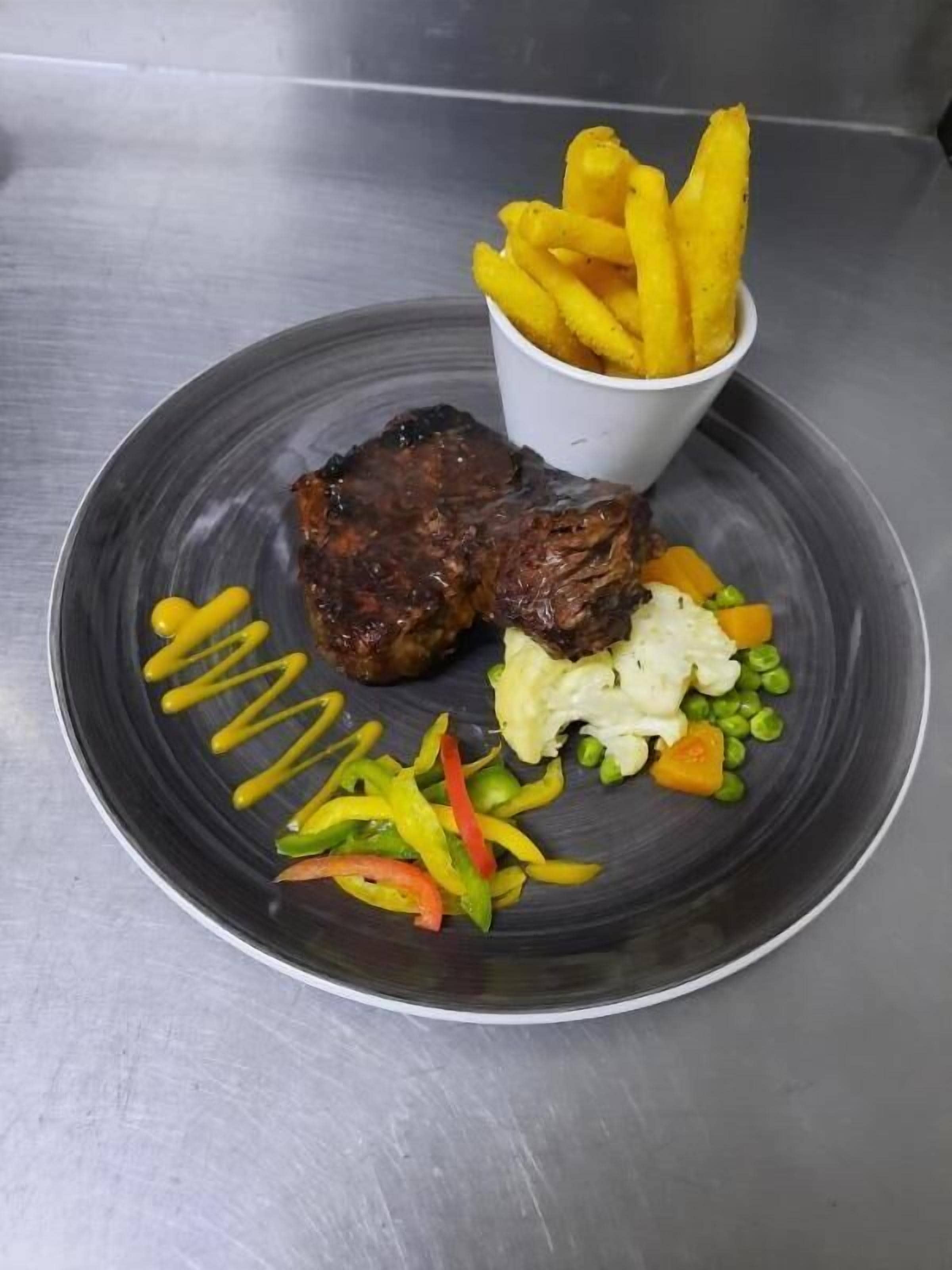 Een bord met een steak, frietjes en een portie gemengde groenten.